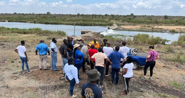 Photo showing people gathering on a field visit by a river.